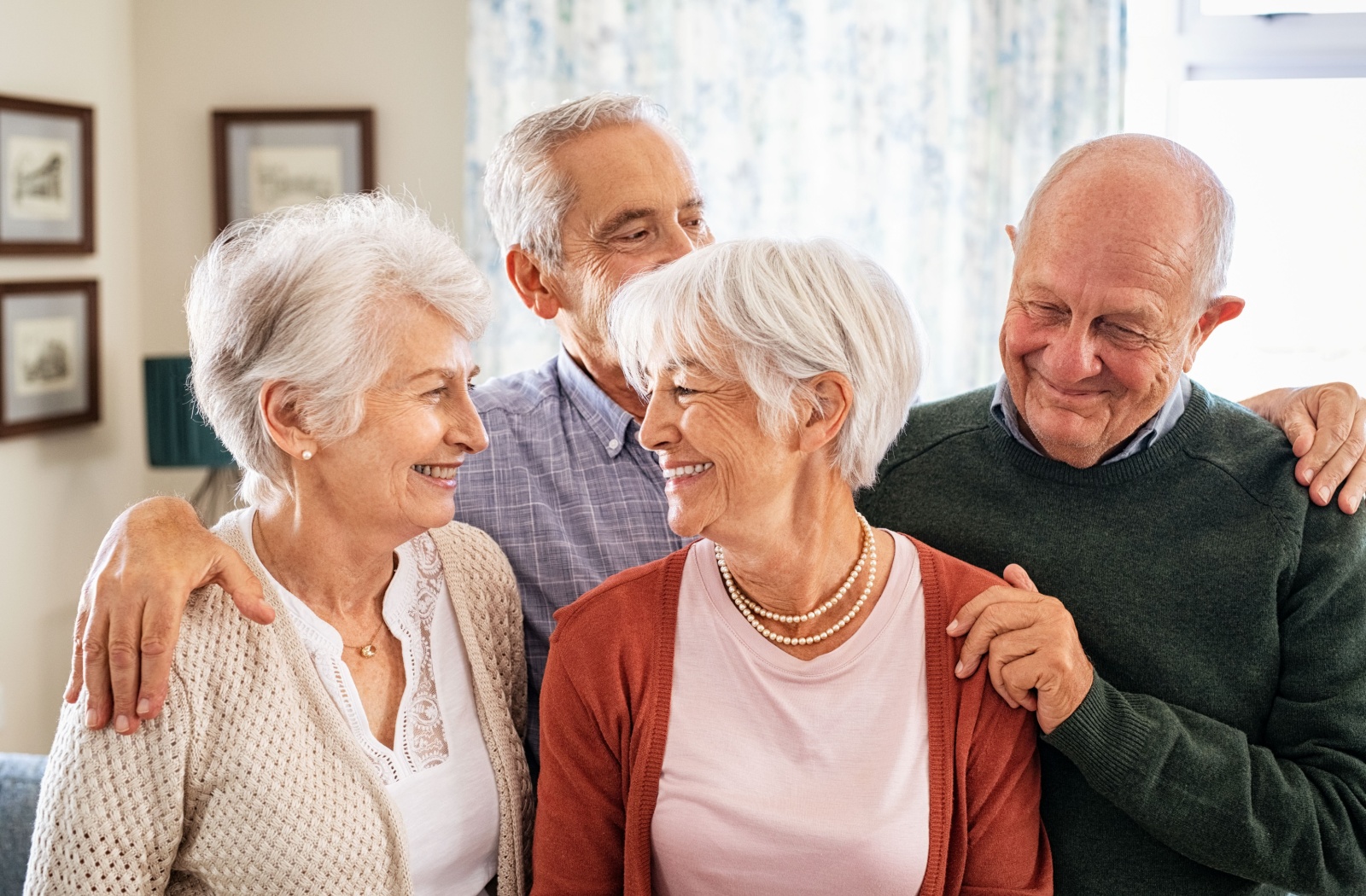 A group of older adults smile and look at one another while posing for a picture together in a common area of their senior living community
