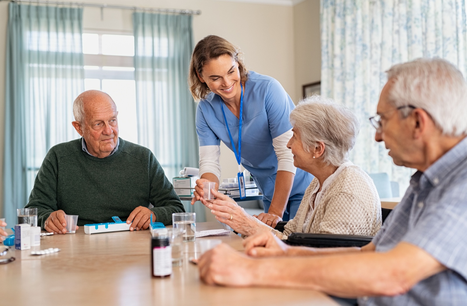 A caregiver hands a group of older adults a cup of water in assisted living to help them with their medications.