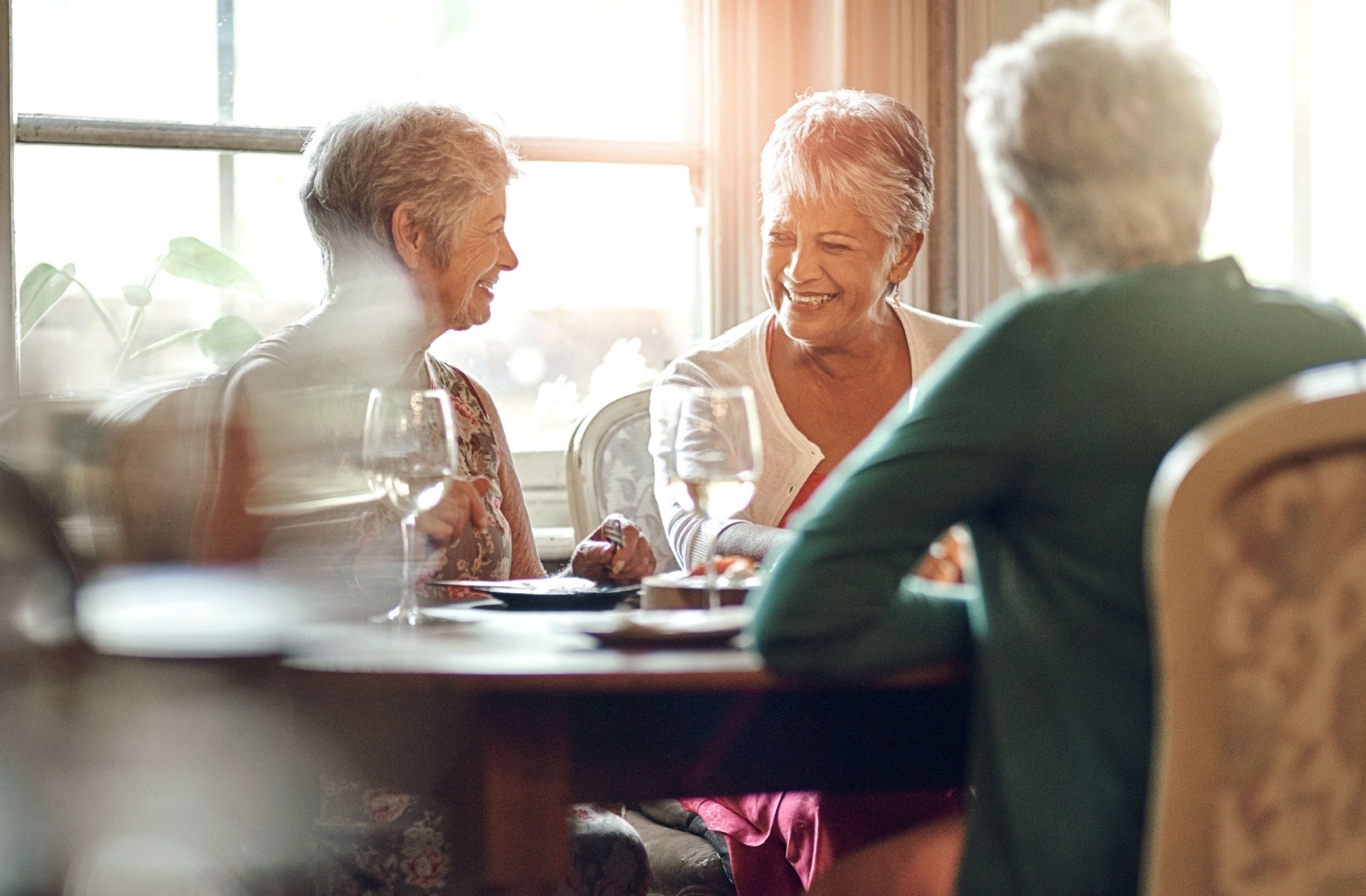 A group of seniors sit at a table in a senior living community and smile as they reminisce.
