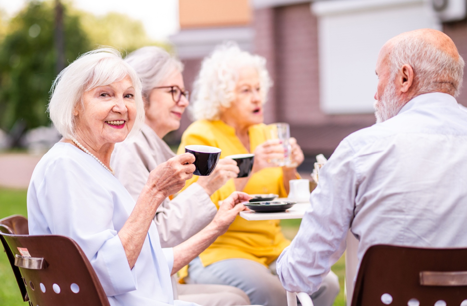 A group of senior friends share coffee while sitting outside at a table.